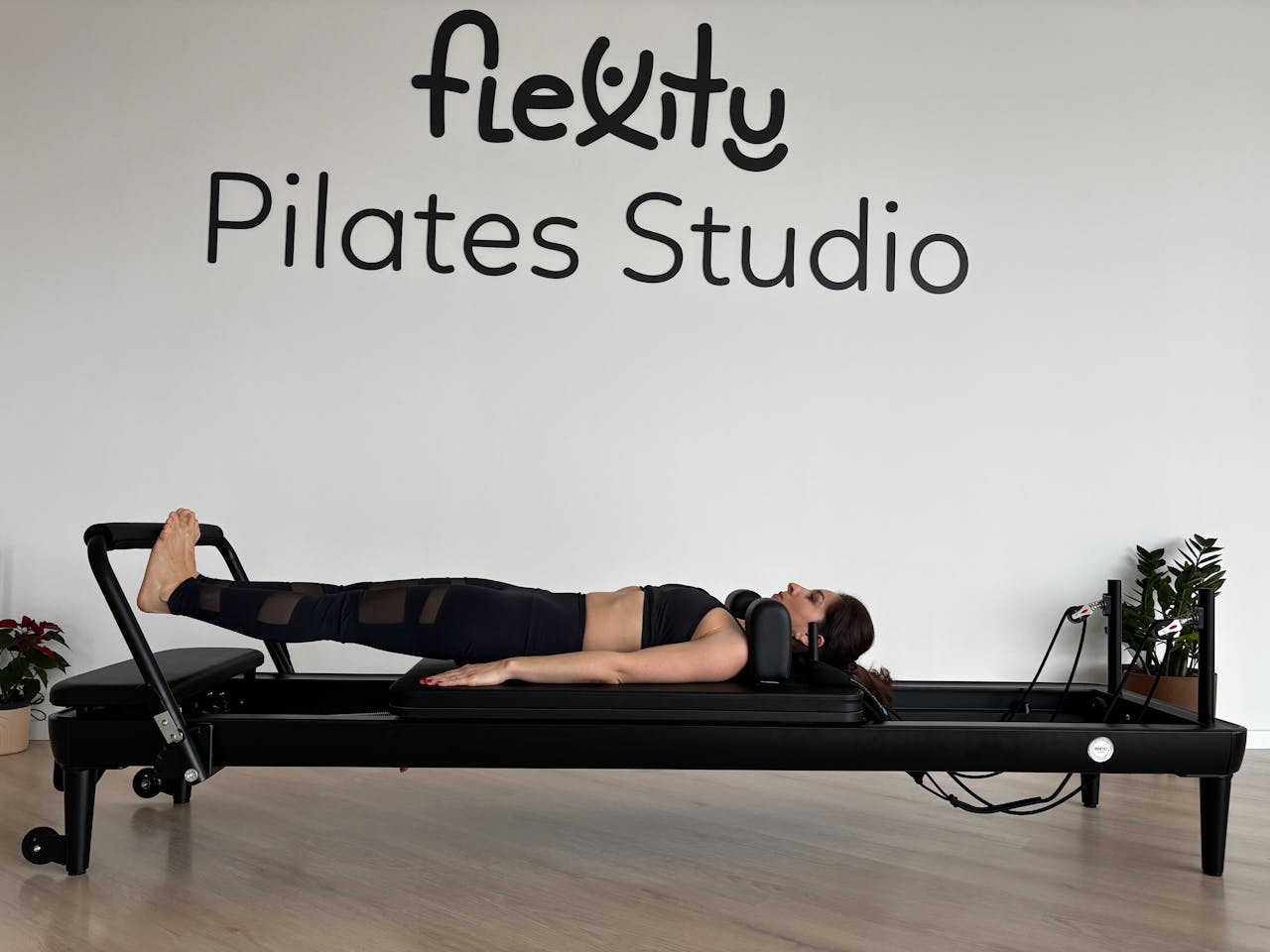 Adult woman exercising on a Pilates reformer at Flexity Pilates Studio indoors.
